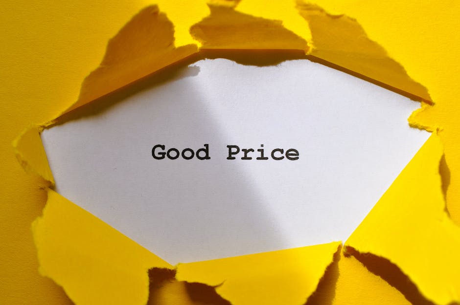 A white piece of paper with the words 'Good Price' printed in black is visible through a torn hole in bright yellow paper or cardboard, creating a rough, jagged opening. The torn edges around the hole are uneven and textured, revealing the interior surface beneath. The scene appears to be indoors with even, neutral lighting. This image may symbolize affordability or value in the context of house removals or moving services, such as those offered by Man With a Van East Ham, emphasizing cost-effective home relocation and furniture transport solutions. The focus is on the contrast between the vibrant yellow exterior and the simple, clear message on the white paper, aligning with concepts of transparent pricing and efficient packing and moving processes.