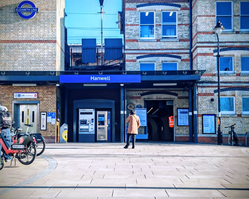 A nighttime view of East Ham railway station platform showing empty train tracks and a covered waiting area with brick walls and large windows. The platform has a yellow safety line and tactile paving